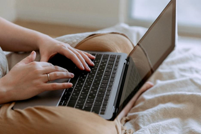 A person sitting on a bed working on a laptop to figure out how to generate more leads.