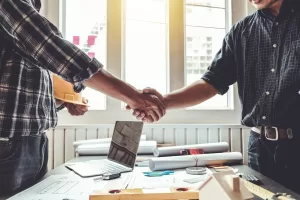 a contractor and a marketing agency owner shaking hands over a desk and a laptop