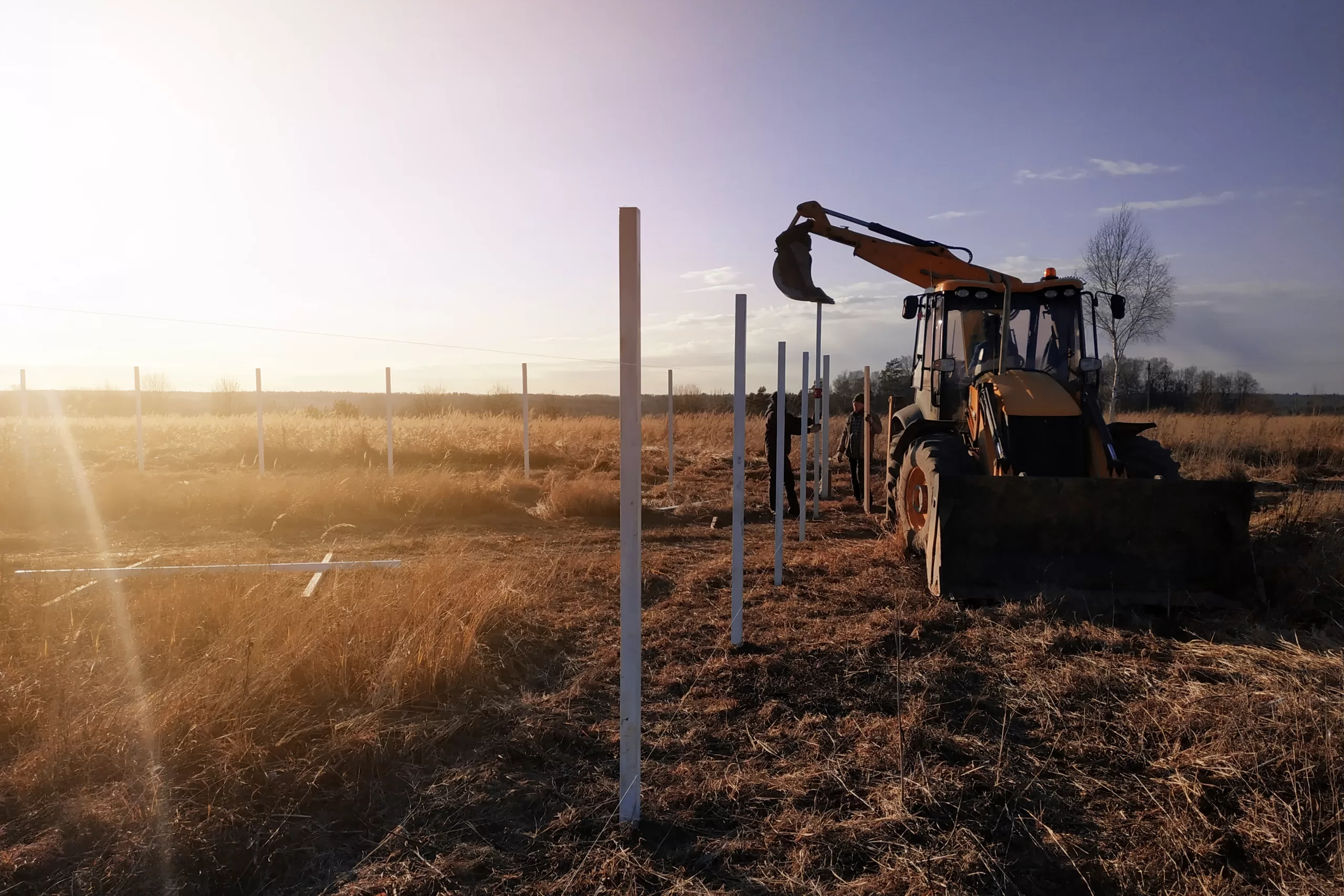 a backhoe assisting in building a fence out in the country at dusk