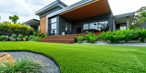 Modern Home Landscaping Design - Search Strategy Marketing - Search Strategy Marketing Modern house with a wooden deck extending to an outdoor seating area, surrounded by lush green lawn and tropical plants.